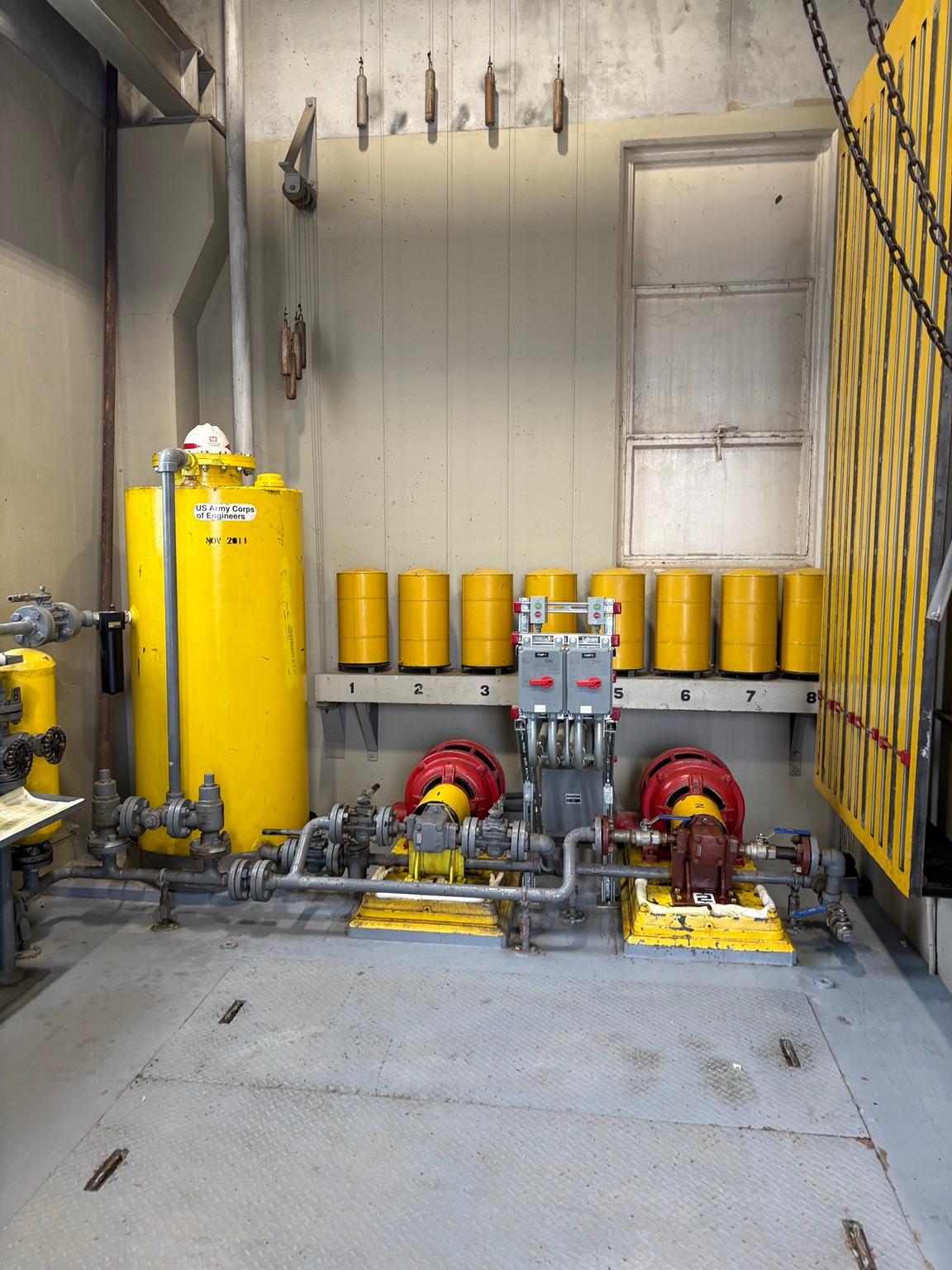 Fueling manifold room with pumps, piping, and yellow storage tanks