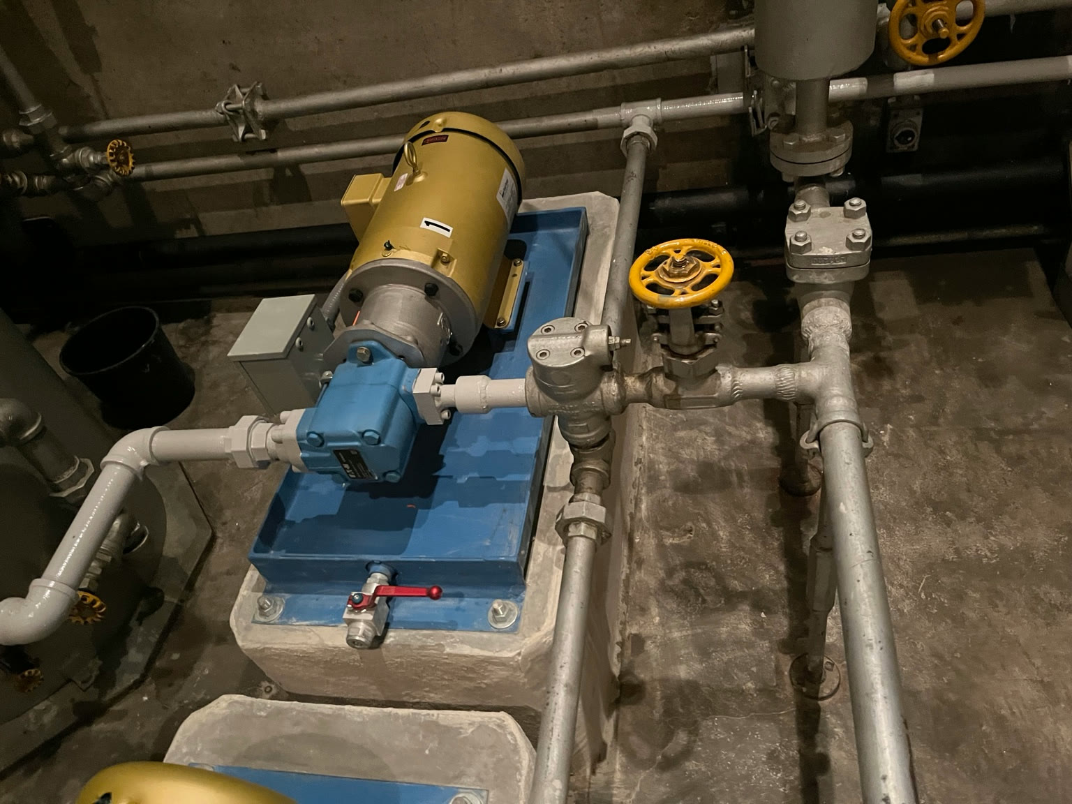 Skid-mounted electric pump and motor assembly connected to transfer piping and yellow-handwheel valves on a concrete pad