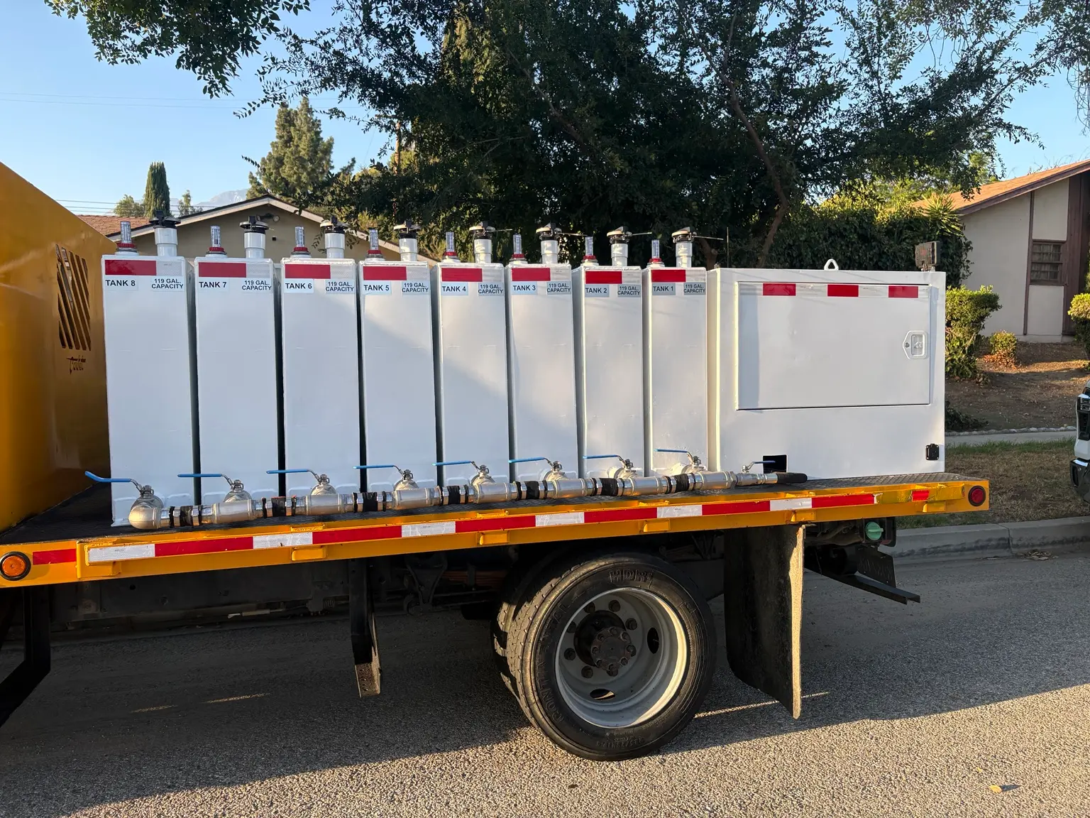 Mobile fuel distribution truck carrying eight labeled 119-gallon tanks on a manifold system
